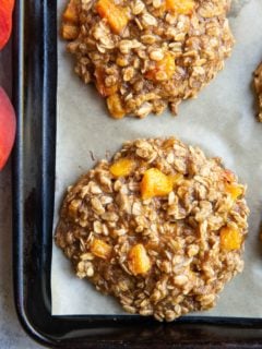 Peach oatmeal cookies on a baking sheet, fresh out of the oven with fresh peaches to the side.