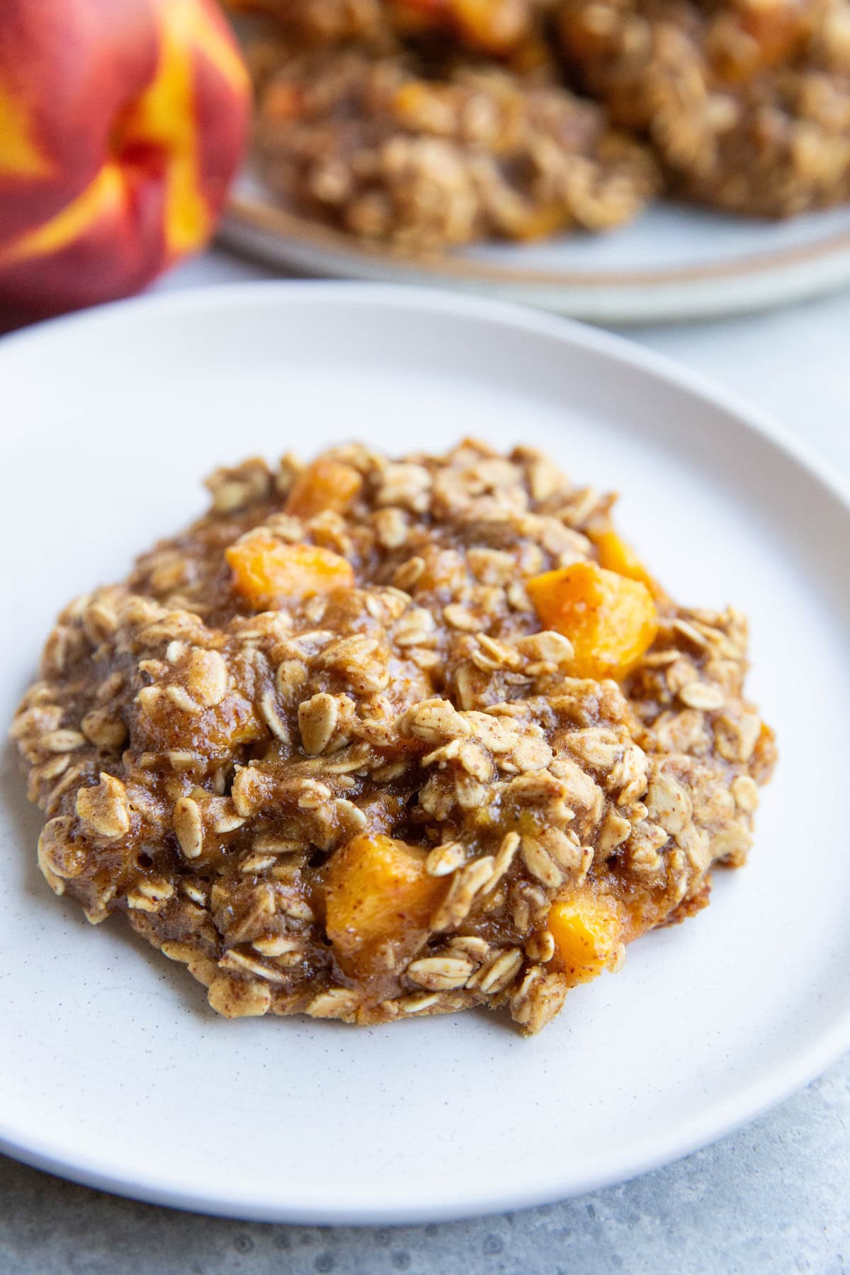 One peach cookie on a white plate with a plate of more peach cookies in the background.