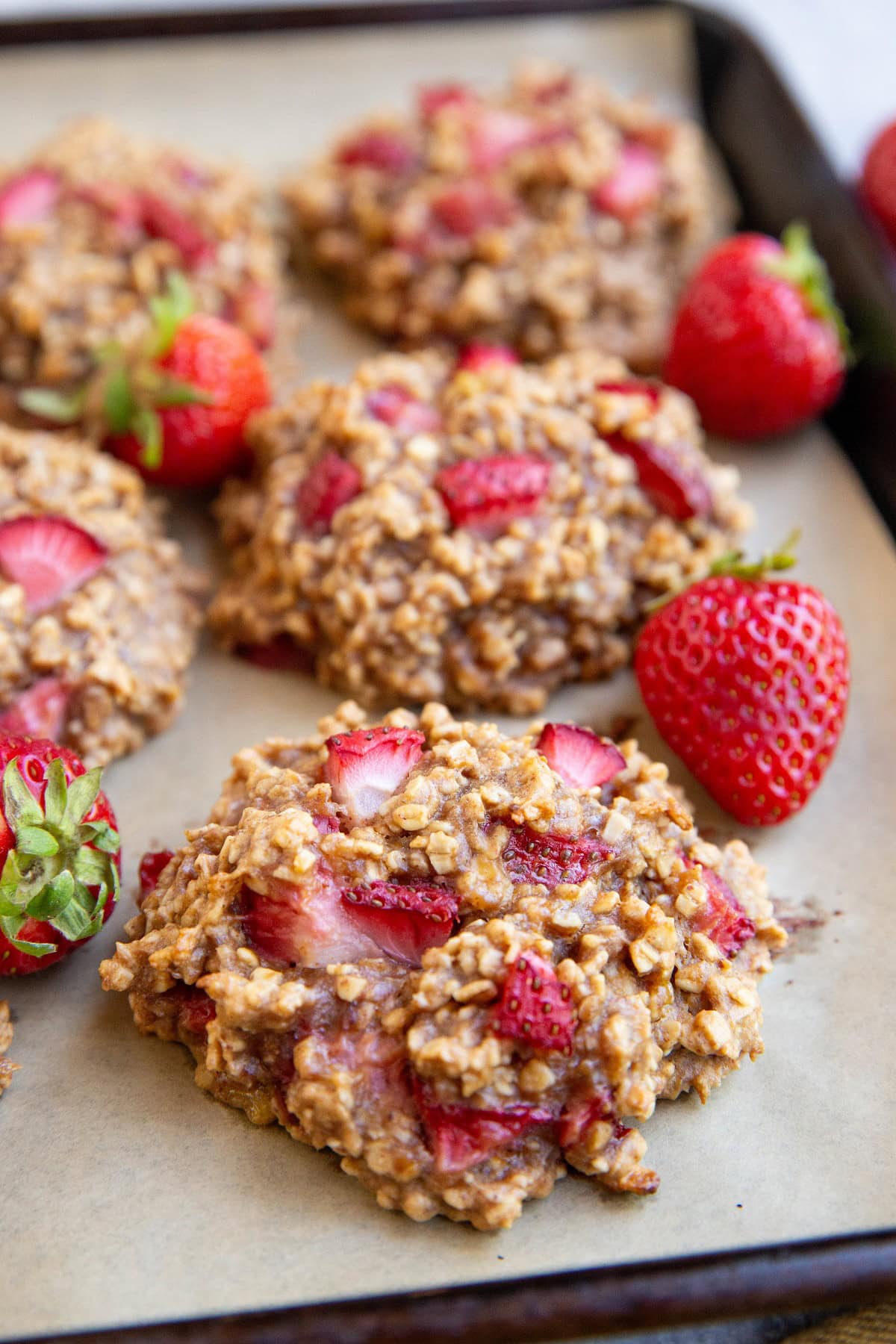 Strawberry cookies on a baking sheet with fresh strawberries all around.