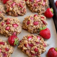 Baking sheet full of strawberry cookies with fresh strawberries all around.