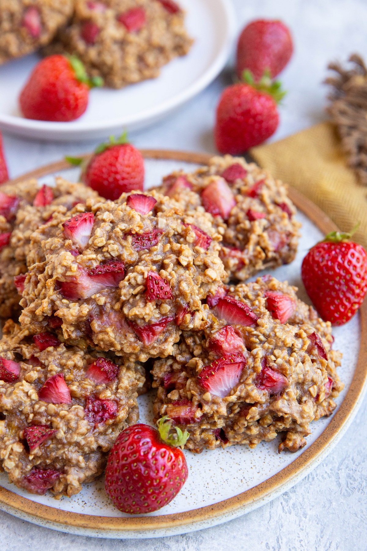 Plate of strawberry oatmeal cookies with a napkin and fresh strawberries all around.