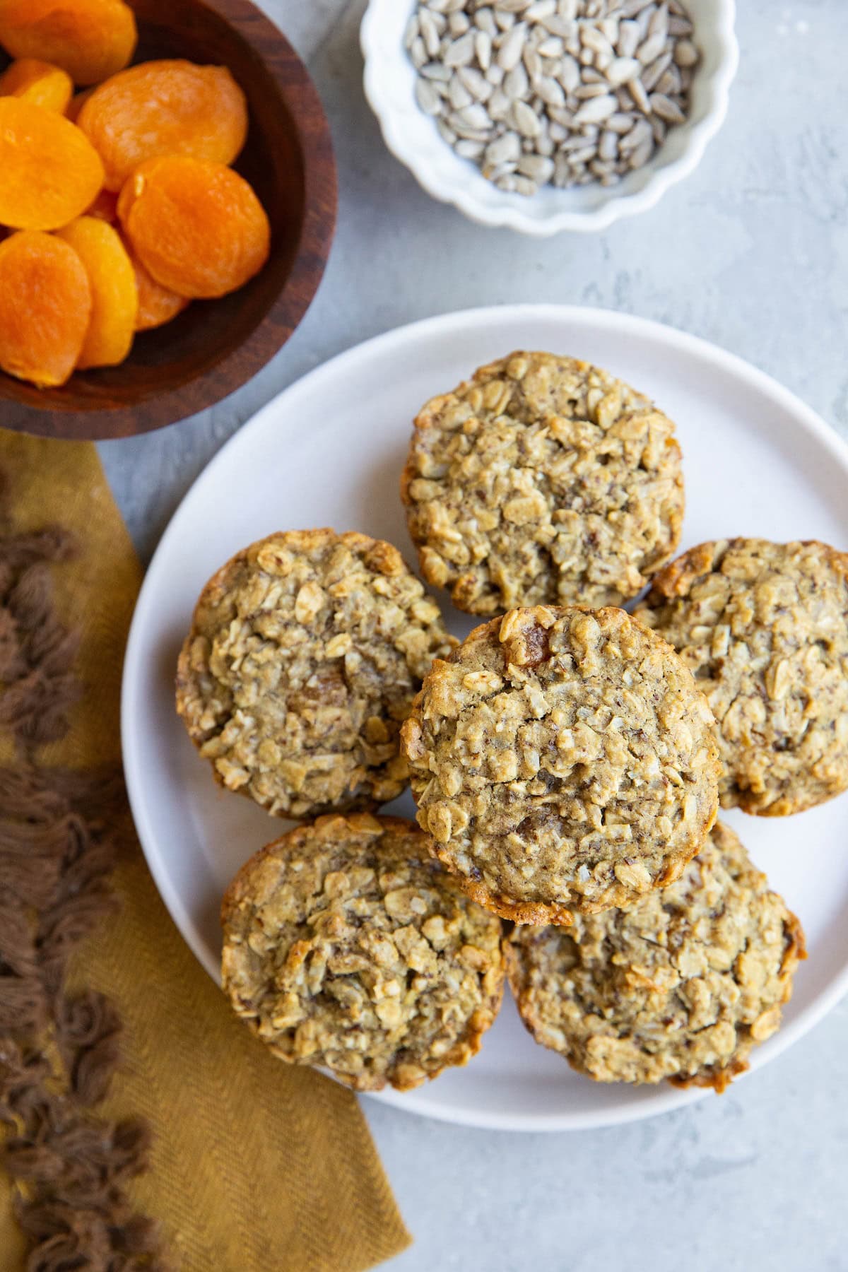 White plate of Aussie bites with a bowl of sunflower seeds and a bowl of dried apricots to the side.