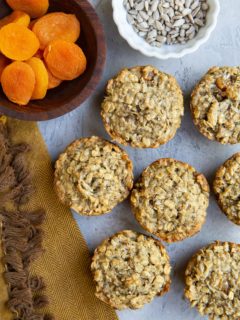 Aussie bites on a blue background with a bowl of sunflower seeds, a bowl of dried apricots, and a golden napkin to the side.