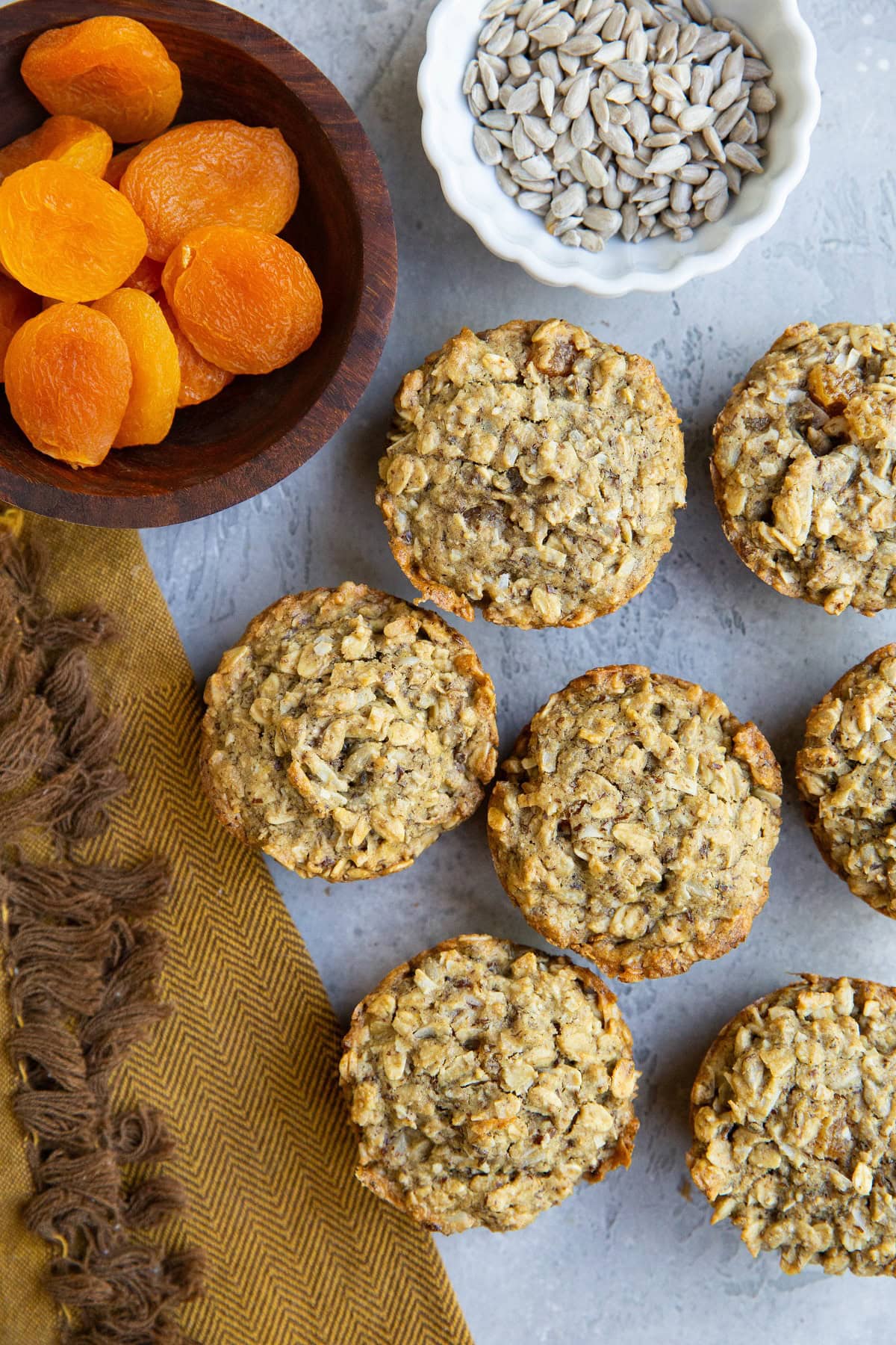 Aussie bites on a blue background with a bowl of sunflower seeds, a bowl of dried apricots, and a golden napkin to the side.