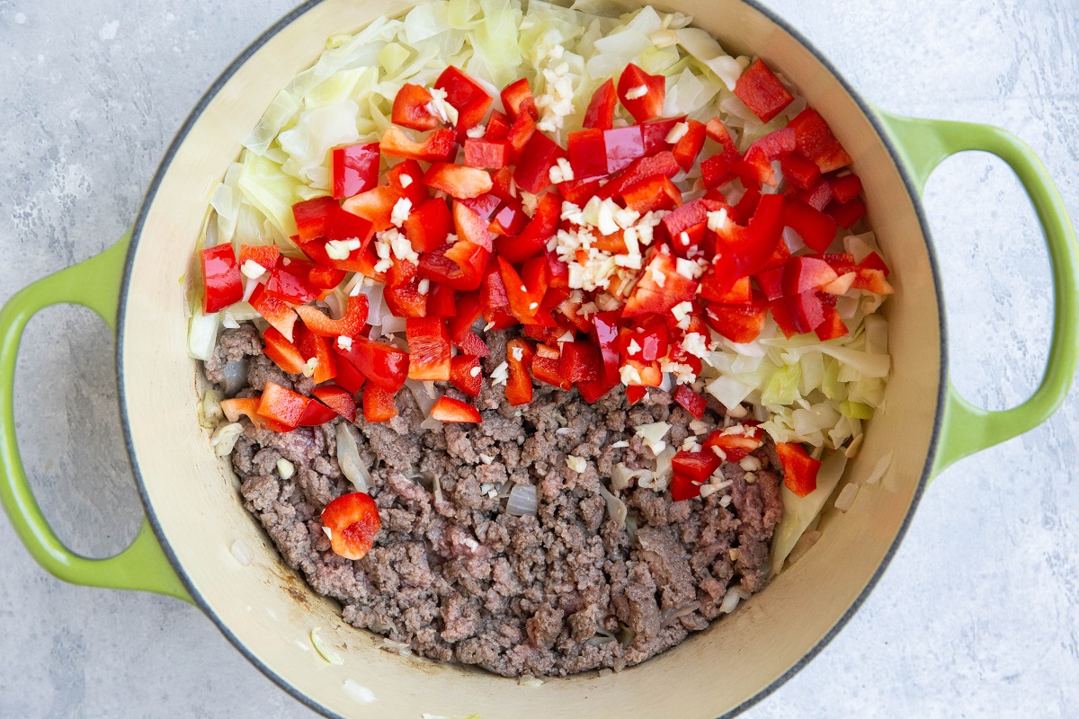 Red bell pepper, garlic, ground beef and cabbage in a large pot.