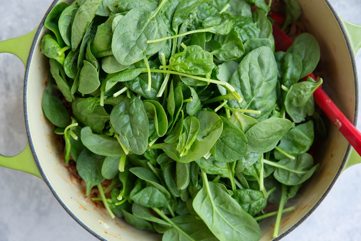 Baby spinach on top of meat and vegetables in a large pot, ready to be mixed in.