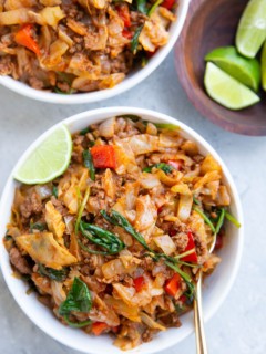 Two white bowls of Mexican ground beef and cabbage with fresh limes to the side.