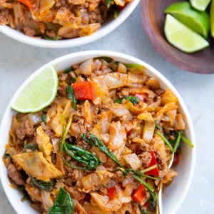 Two white bowls of Mexican ground beef and cabbage with fresh limes to the side.