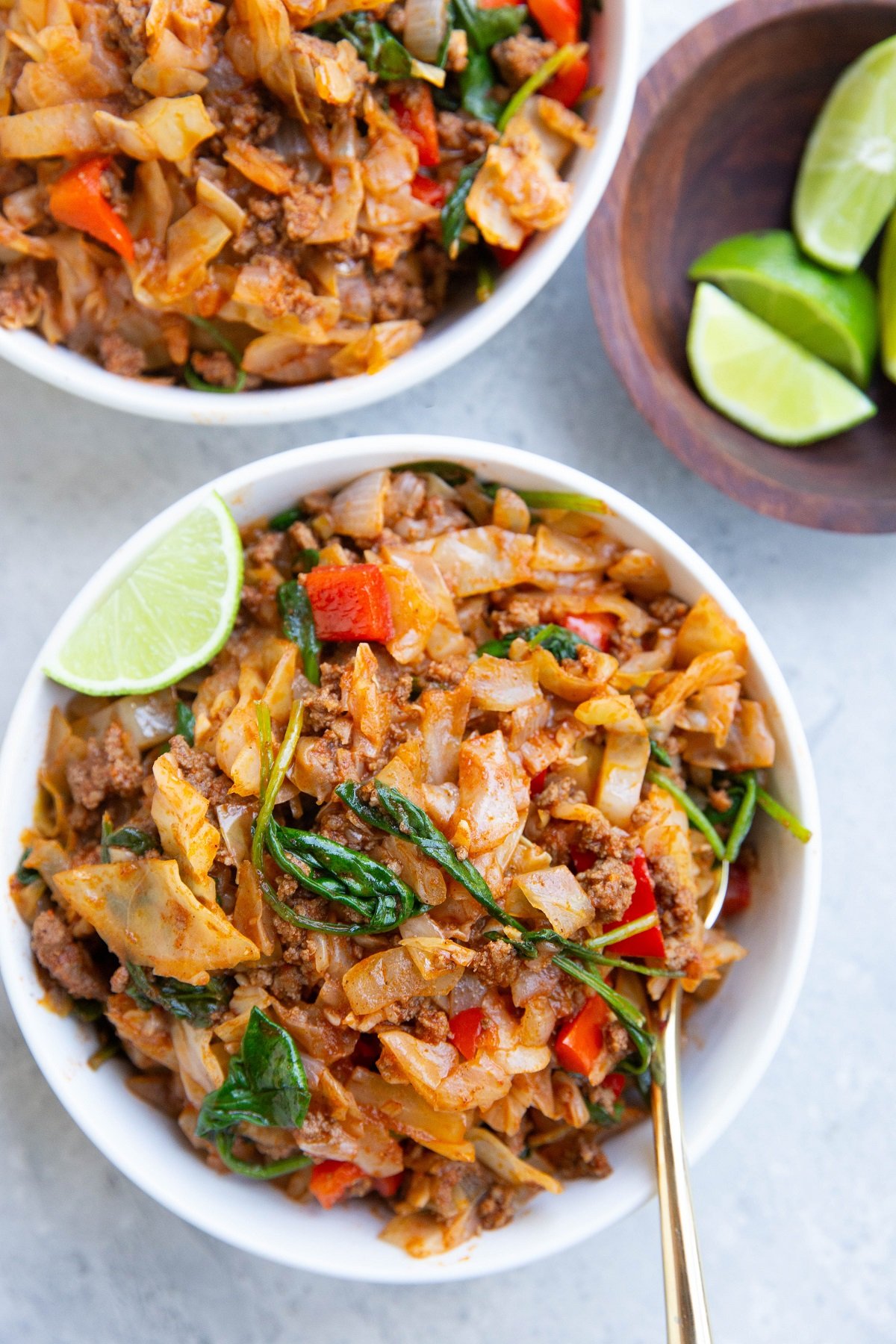 Two white bowls of Mexican ground beef and cabbage with fresh limes to the side.