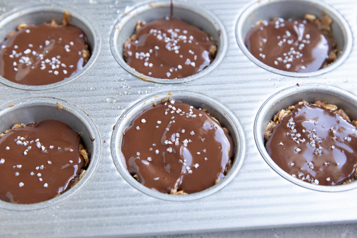 Peanut butter oatmeal layer with melted chocolate on top and flaky sea salt sprinkled on top inside of a muffin tray.