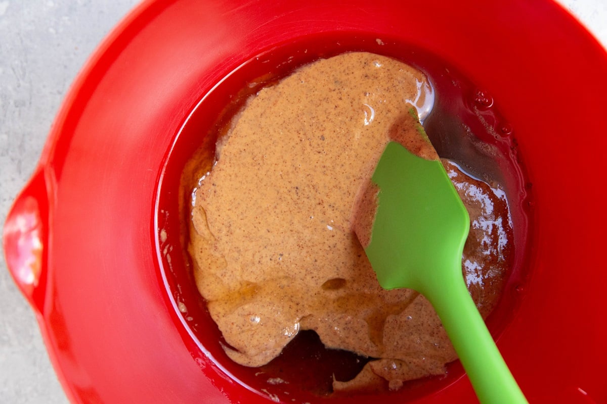 Pure maple syrup and peanut butter in a red mixing bowl to make peanut butter cups.