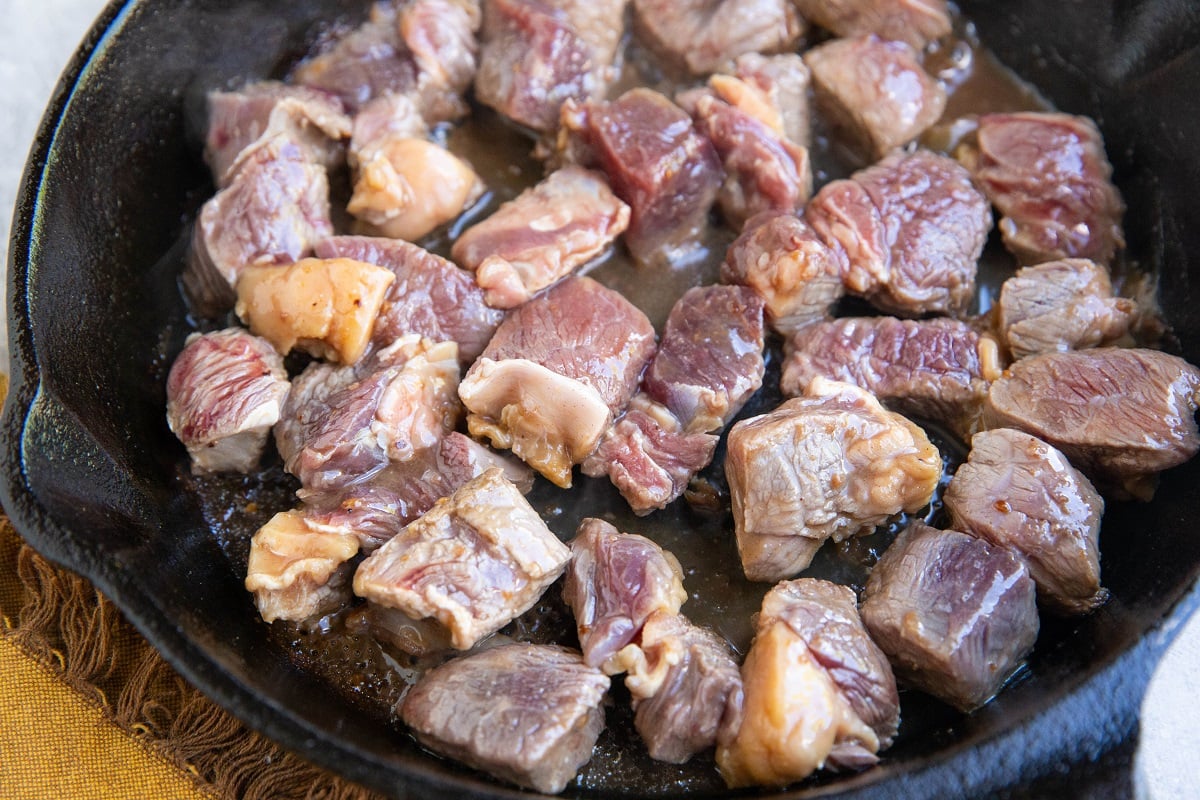 Steak bites cooking in a cast iron skillet.