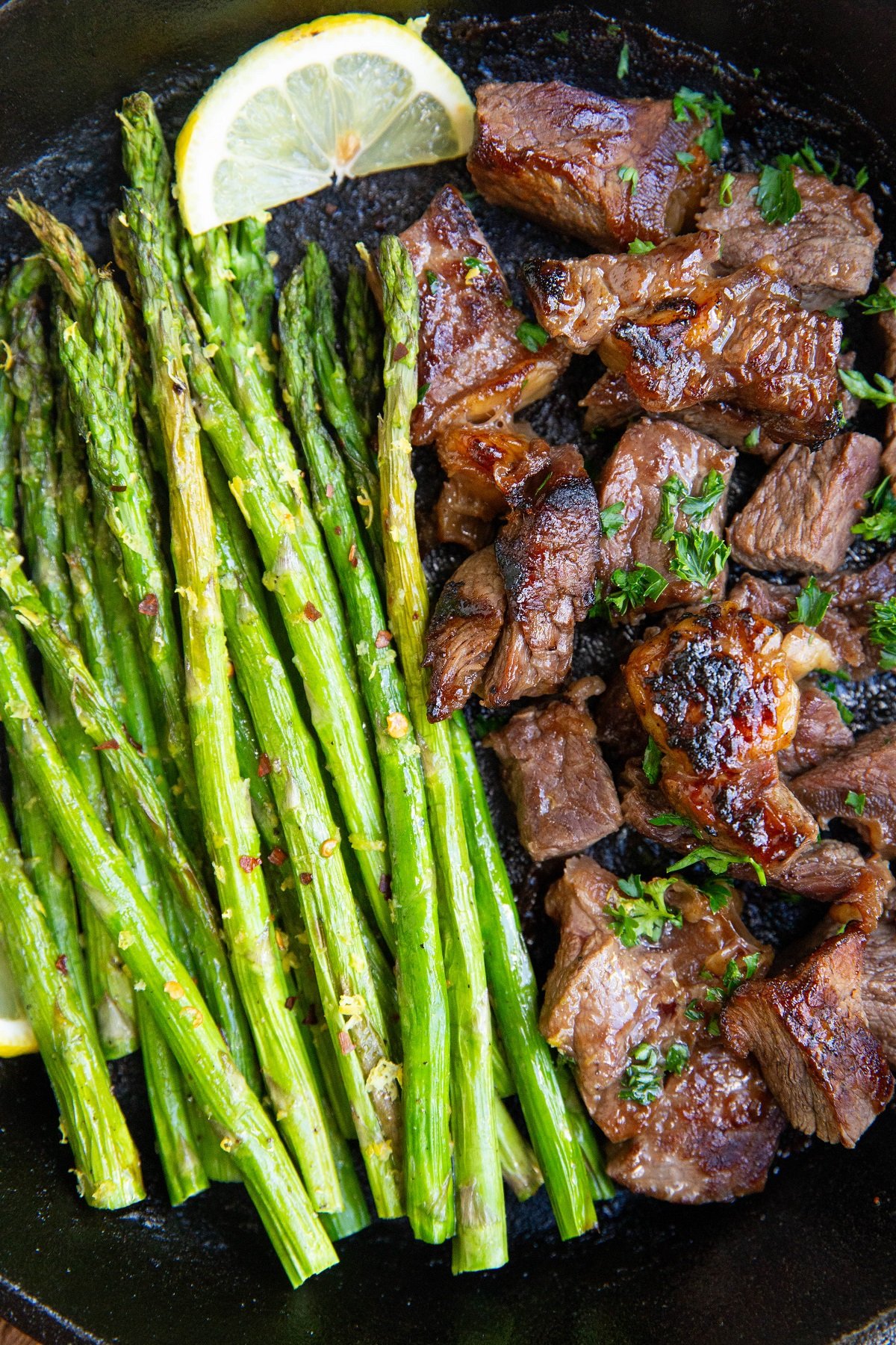 Cast iron skillet with steak bites and asparagus in it, ready to eat.