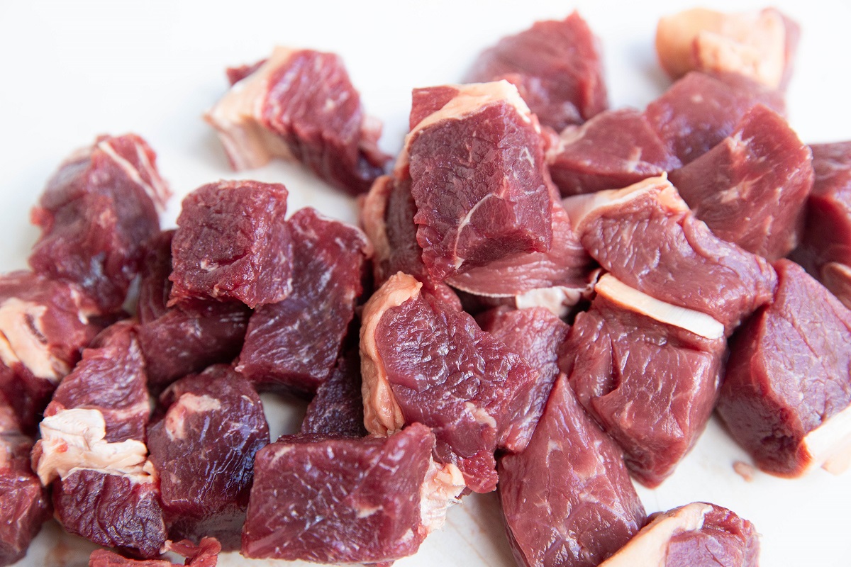 Steak chopped into cubes on a white cutting board.