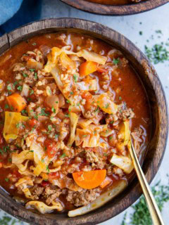 Big wooden bowl of unstuffed cabbage soup with a blue napkin to the side and dried herbs.