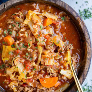 Big wooden bowl of unstuffed cabbage soup with a blue napkin to the side and dried herbs.