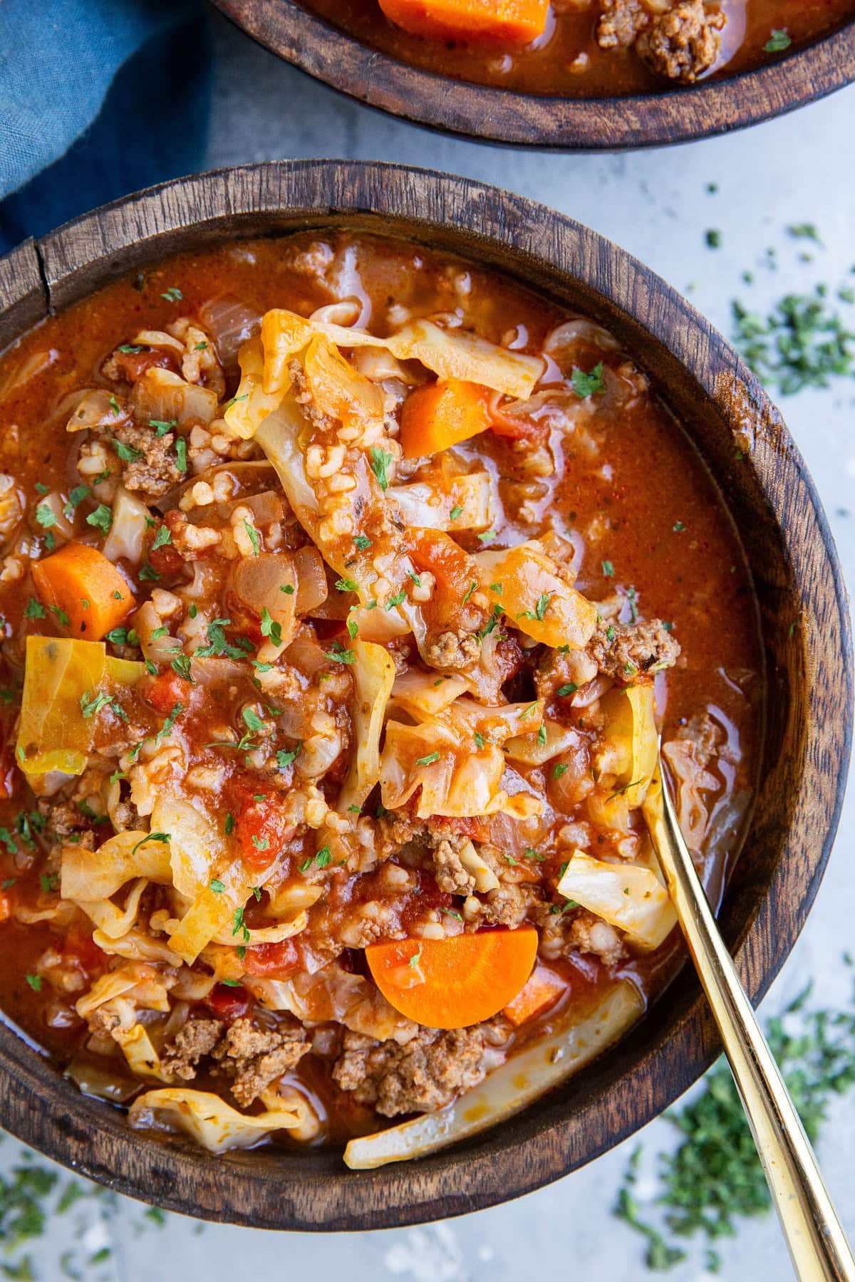 Big wooden bowl of unstuffed cabbage soup with a blue napkin to the side and dried herbs.