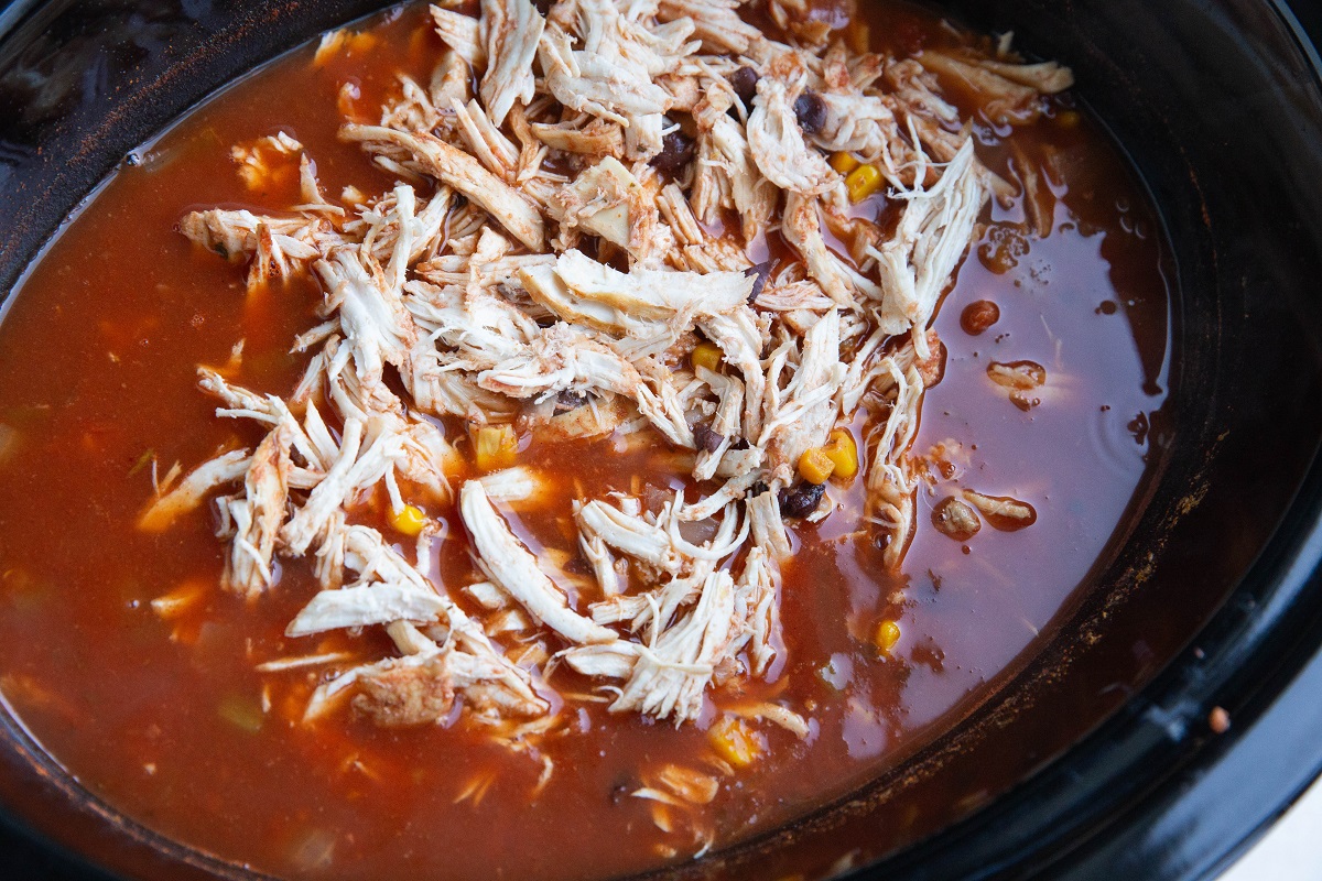 Shredded chicken on top of tortilla soup, ready to be mixed in.
