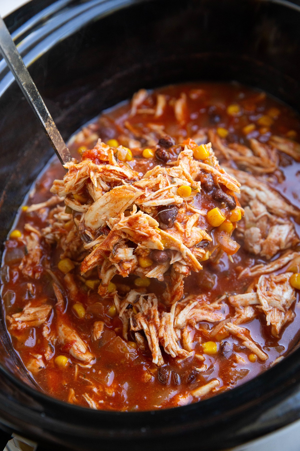 Ladle scooping out a scoop of chicken tortilla soup out of a crock pot.