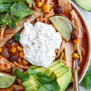 Big white bowl of chicken tortilla soup with avocado, sour cream, homemade tortilla strips and cilantro on top