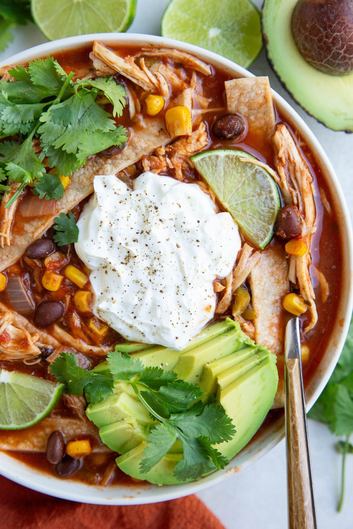 Big white bowl of chicken tortilla soup with avocado, sour cream, homemade tortilla strips and cilantro on top