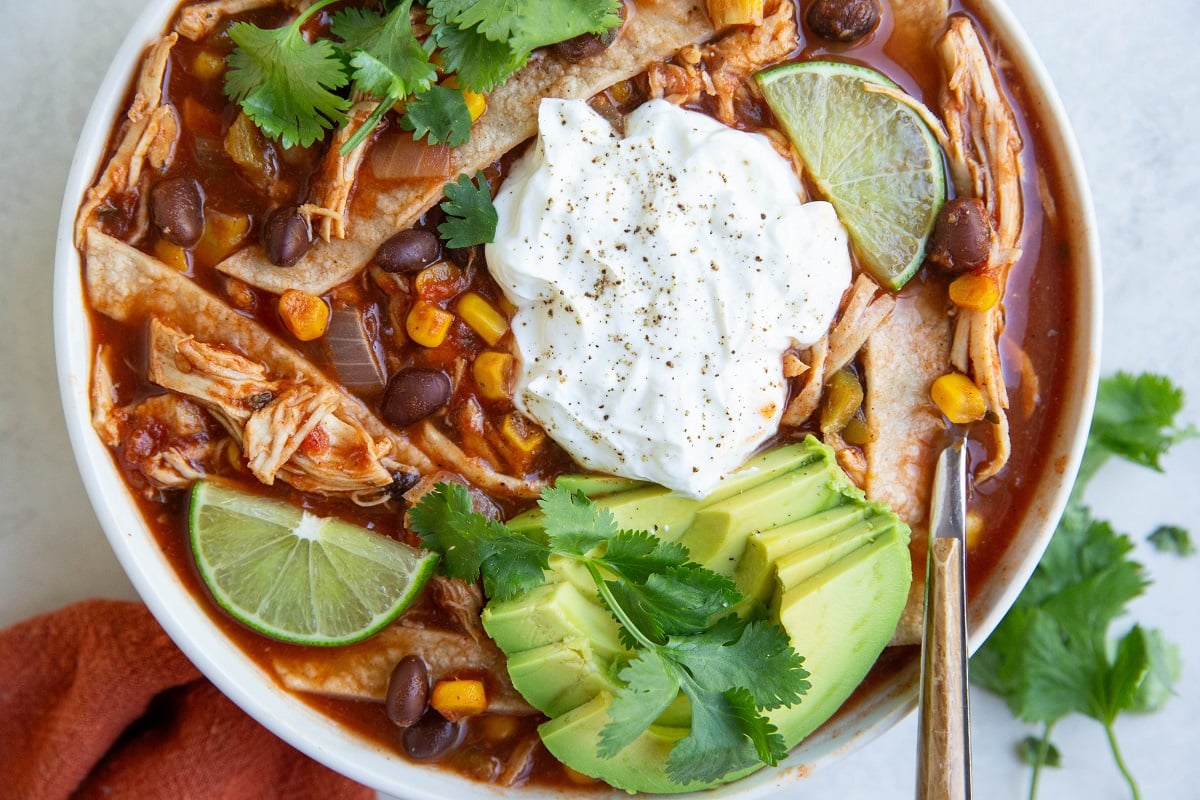 White bowl of chicken tortilla soup with toppings.