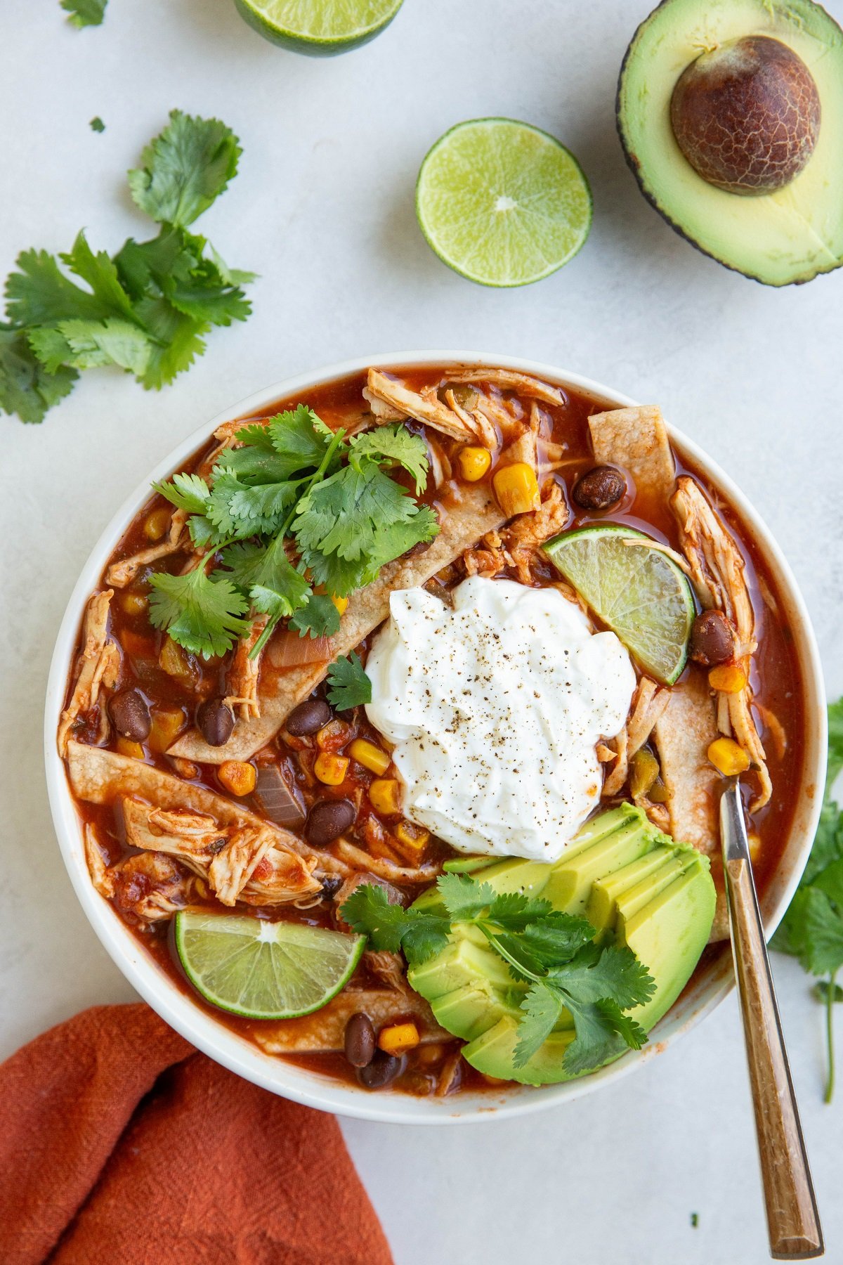 Bowl of chicken tortilla soup with an avocado and limes around the sides.
