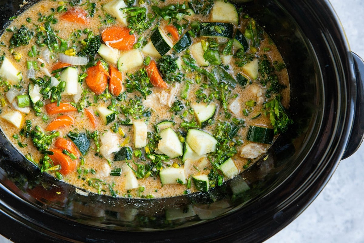 Fresh vegetables stirred into red chicken curry in a slow cooker.