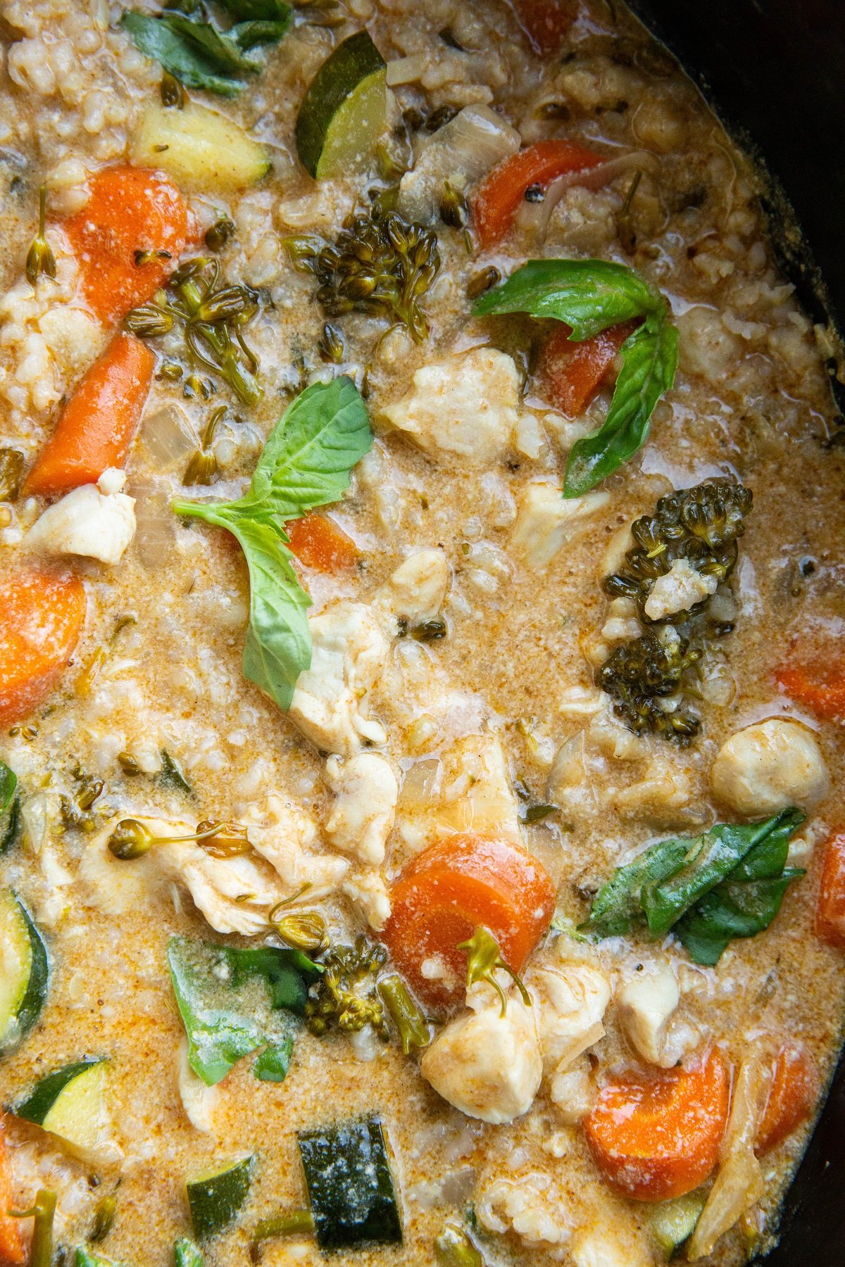 Close up image of chicken curry in a crock pot with veggies and fresh basil mixed in.