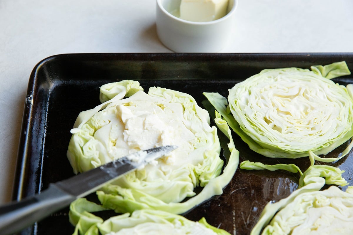 Knife spreading butter over cabbage rounds.