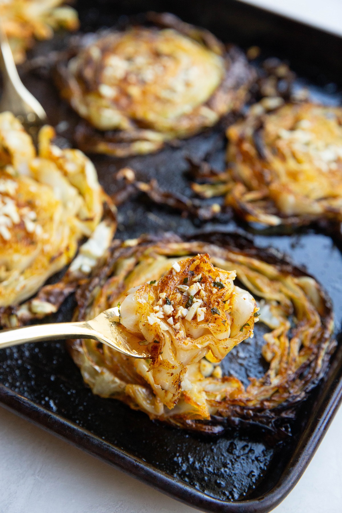 Fork holding some caramelized cabbage off of the baking sheet.