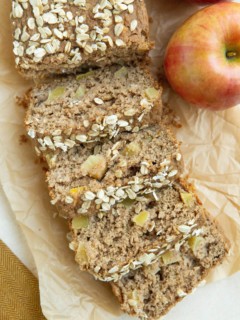 Loaf of apple bread cut into individual slices with apples next to it.