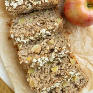 Loaf of apple bread cut into individual slices with apples next to it.