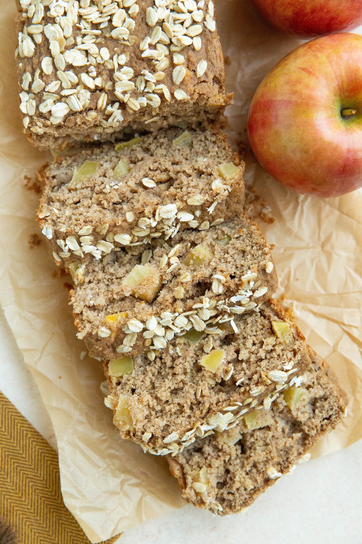 Loaf of apple bread cut into individual slices with apples next to it.