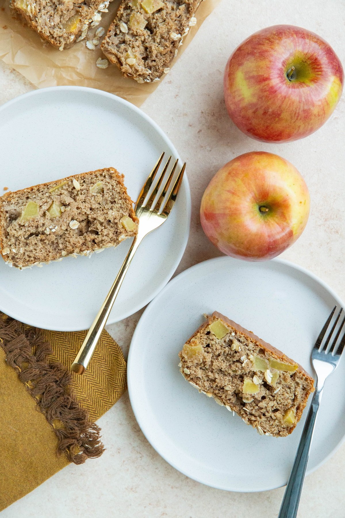 Two white plates with slices of apple bread with fresh apples and a napkin to the side.