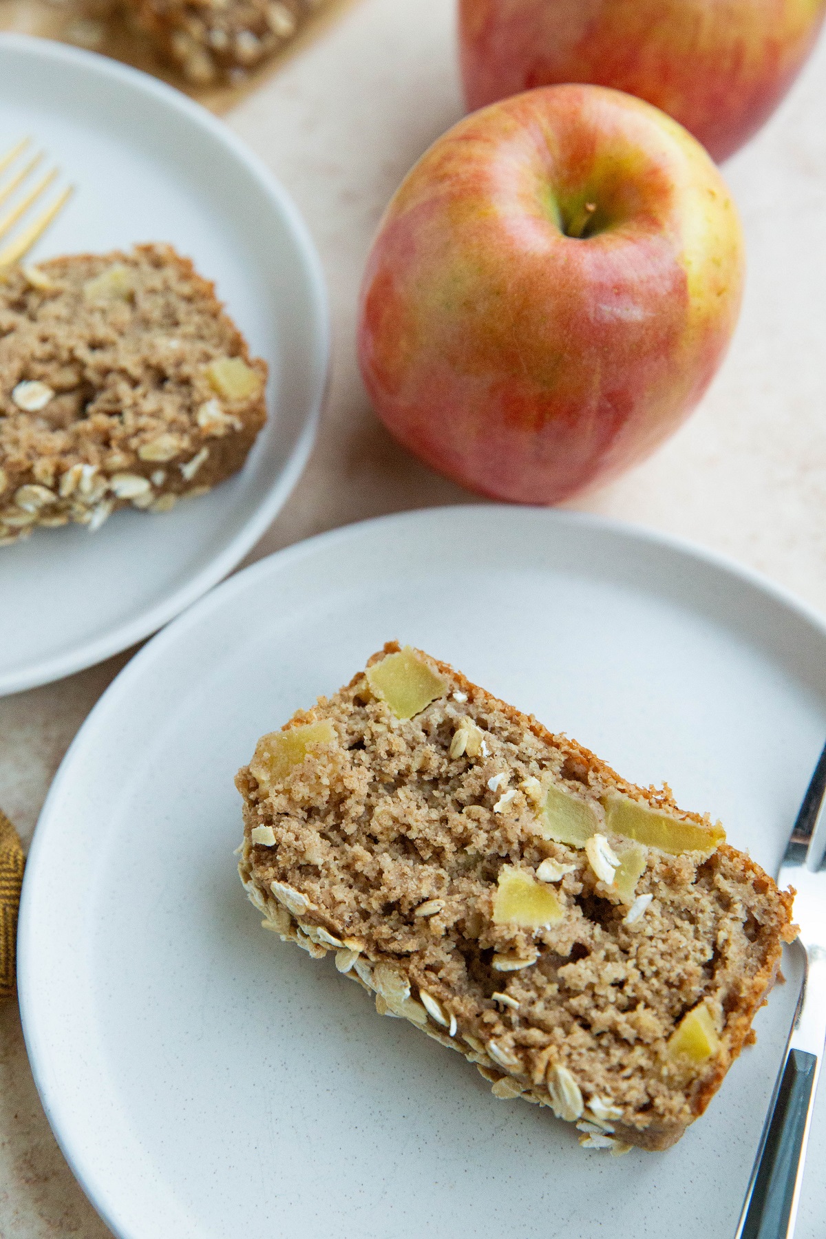 Slices of apple bread on white plates with fresh apples in the background.