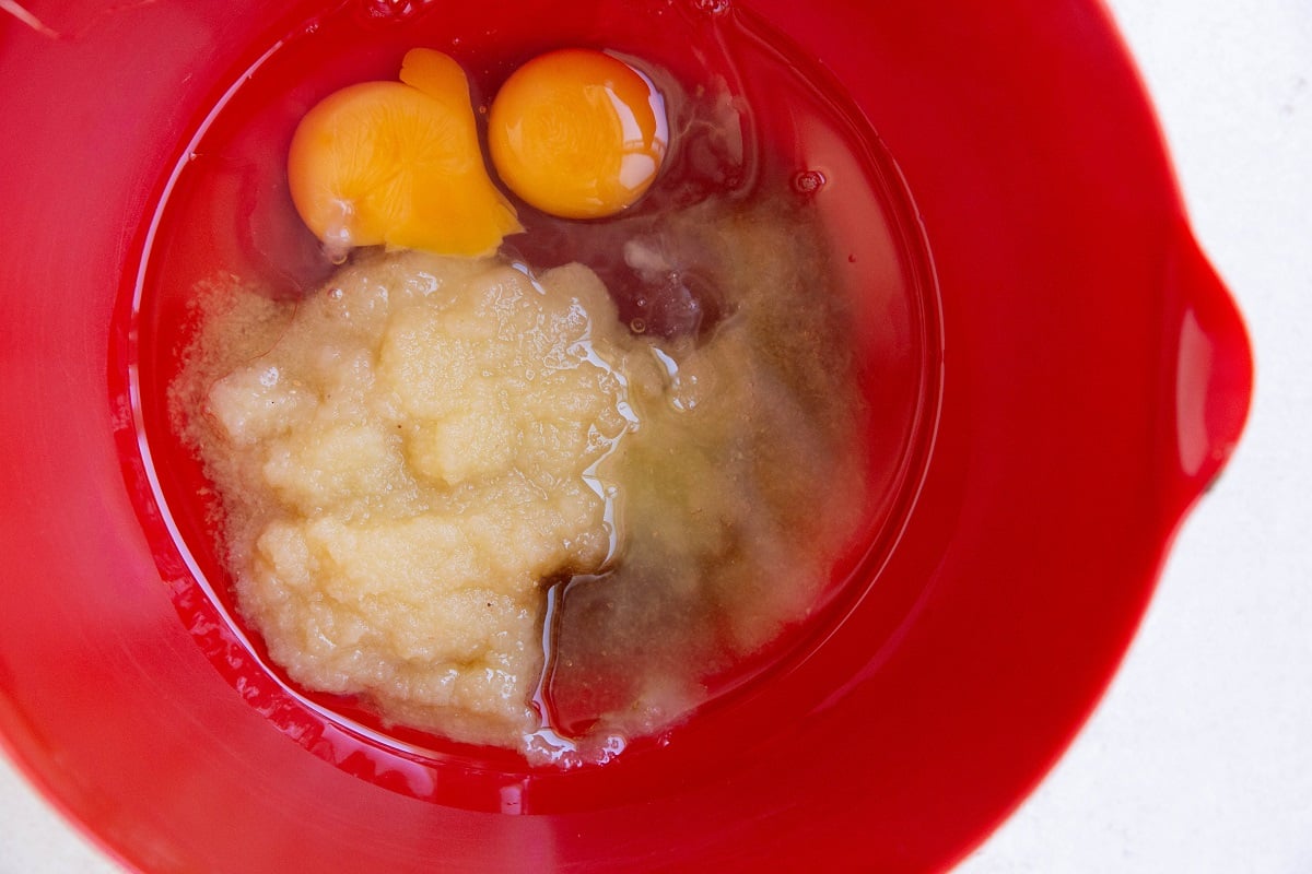 Red bowl with applesauce, eggs, pure maple syrup and vanilla extract.