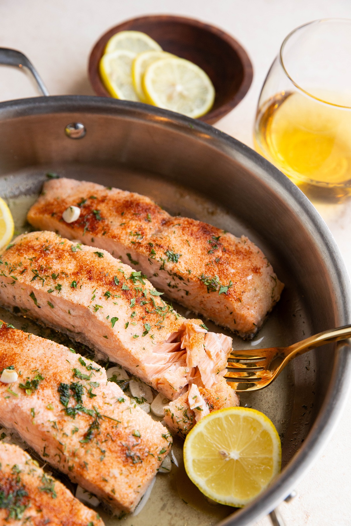 Stainless steel skillet with 4 poached salmon fillets inside and a gold fork taking a bite out of one of the fillets.