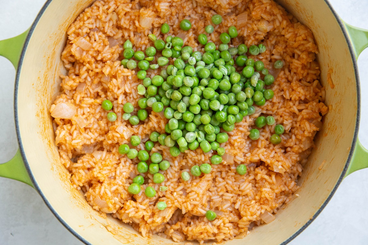 Pot of Mexican rice with green peas on top, ready to be mixed in.