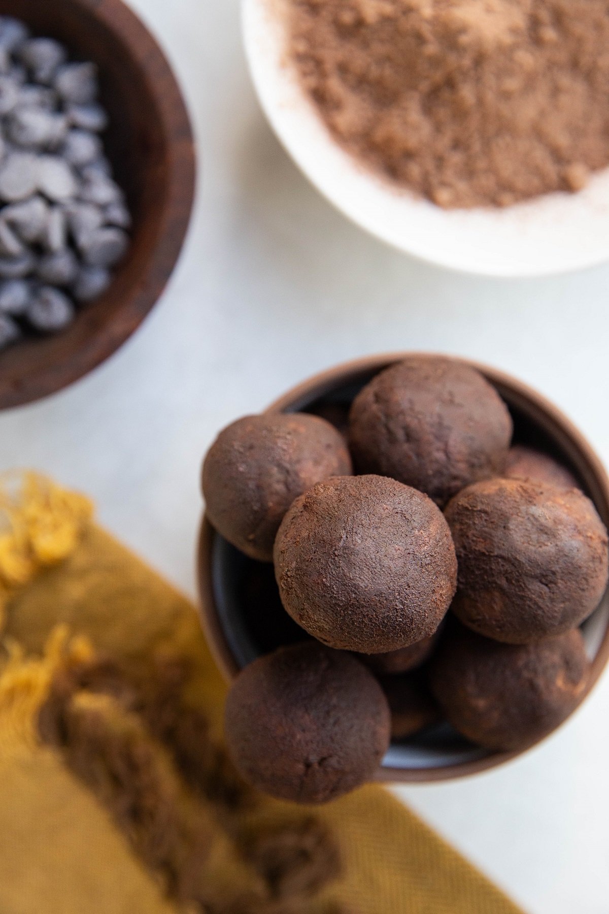 Bowl of protein bites with a bowl of chocolate chips and a bowl of cocoa powder to the side.