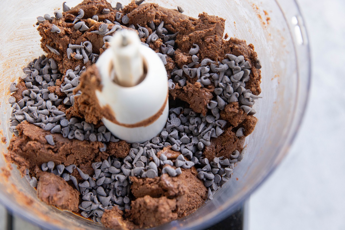 Food processor with brownie bite mixture and chocolate chips on top, ready to be mixed in.