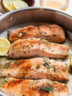 Four cooked salmon filers in a skillet, ready to serve.