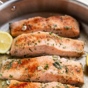 Four cooked salmon filers in a skillet, ready to serve.