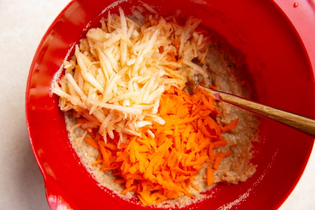 grated apple and grated carrot on top of muffin batter, ready to be mixed in.