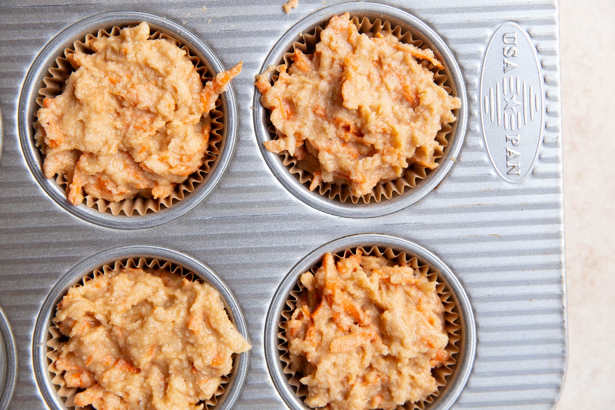 Muffin tin filled with apple carrot muffin batter, ready to bake.