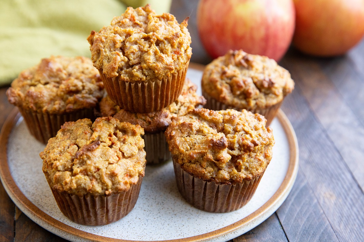 Plate of apple carrot muffins stacked on each other with fresh apples in the background.