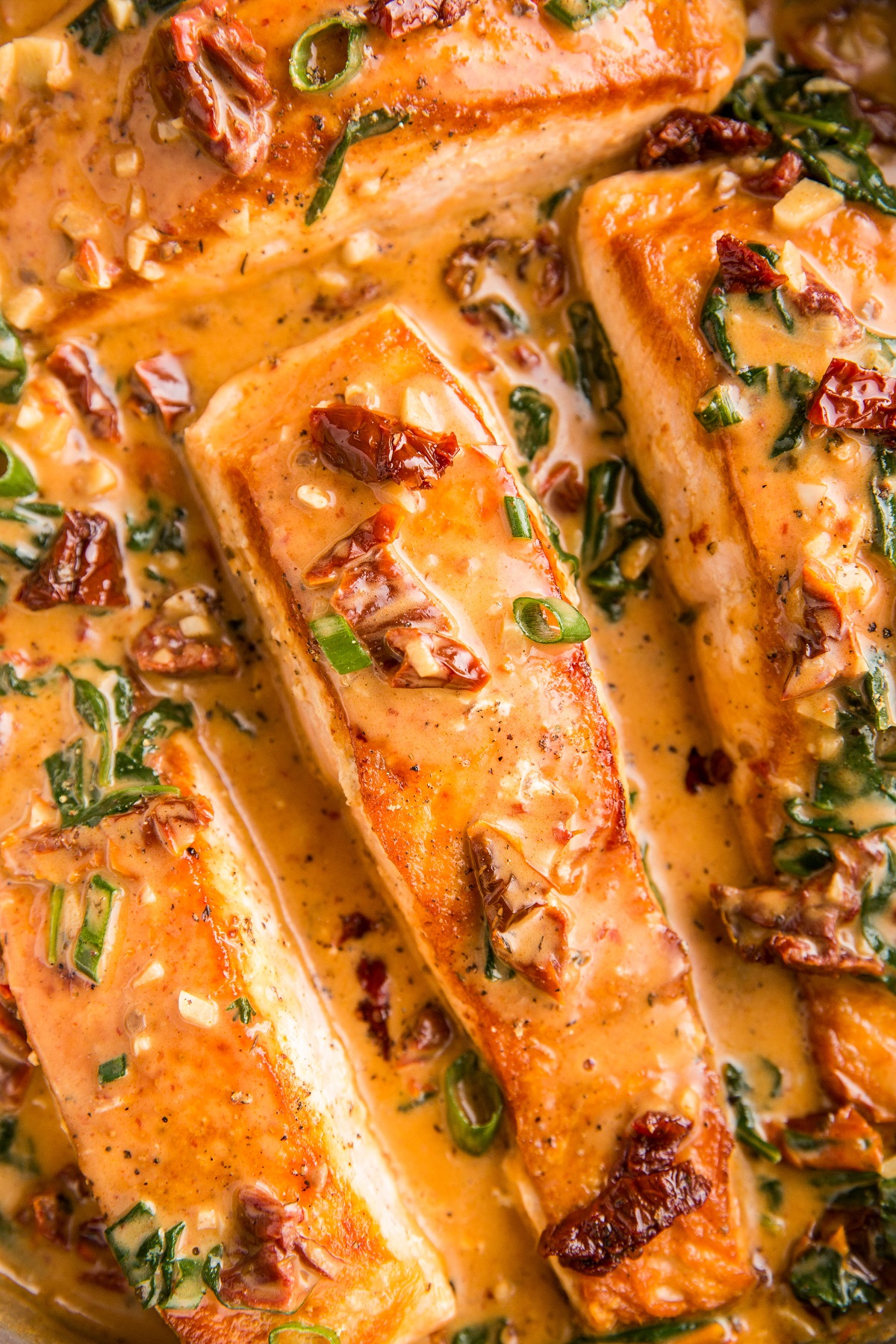 Four salmon filets in a skillet covered with sun-dried tomato sauce.