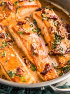 Stainless steel skillet with sun-dried tomato salmon inside and a blue napkin to the side, ready to serve.