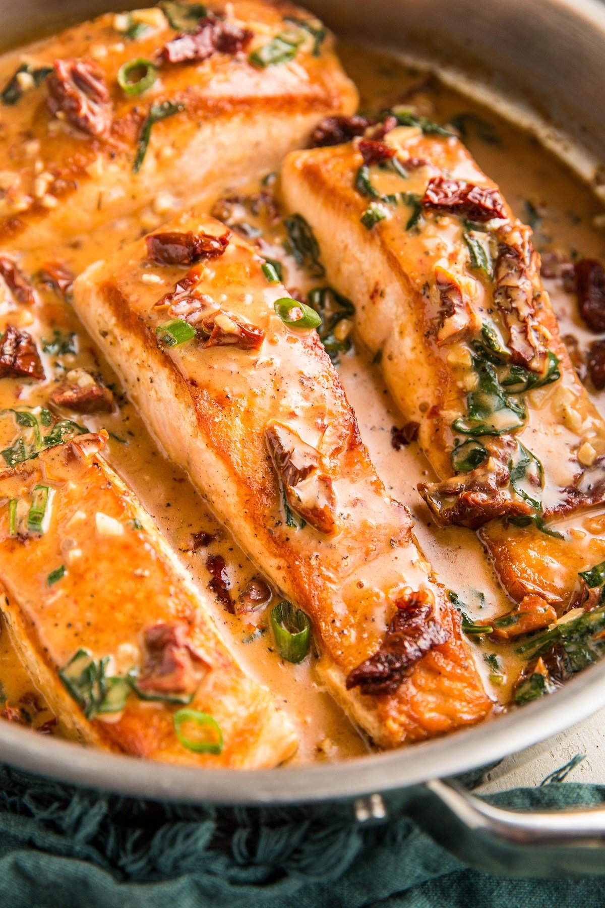 Stainless steel skillet with sun-dried tomato salmon inside and a blue napkin to the side, ready to serve.