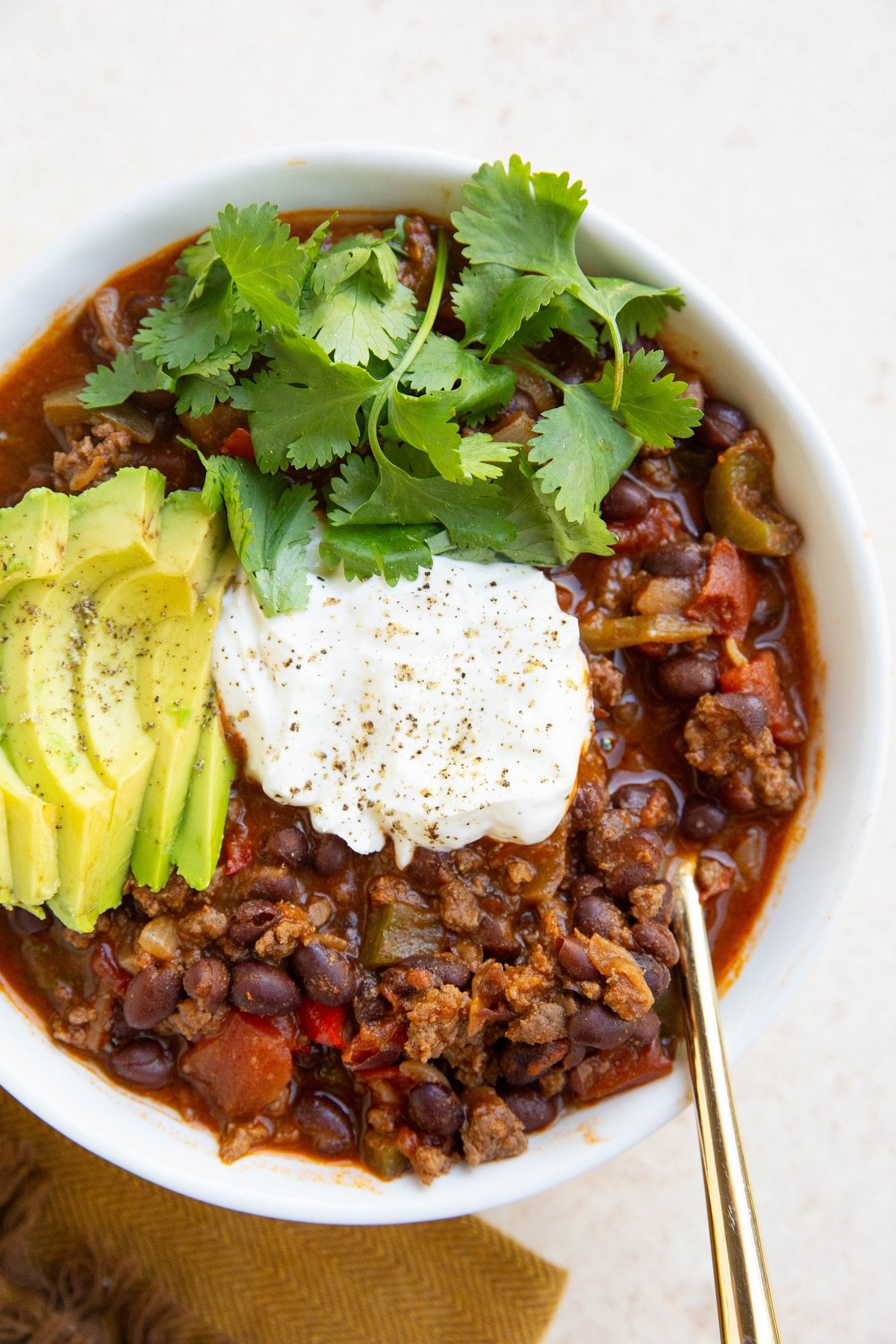 Big bowl of deer chili with sour cream, cilantro and sliced avocado on top.